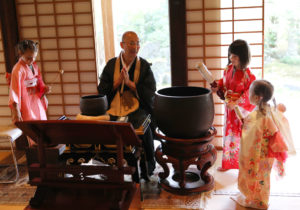 girls in kimono trying to ring a big bell in a temple